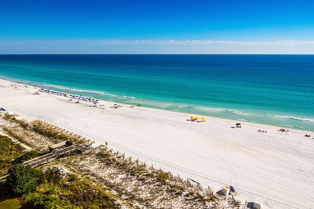 Quiet sugar-white sand beach on 30A in fall with emerald-green Gulf waters and sunny skies